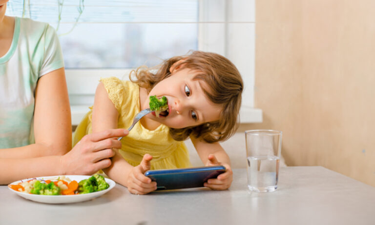 een kind met zijn smartphone aan tafel tijdens het familiediner wordt afgeleid door peppa pig of een andere youtube video